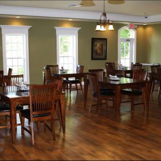 An empty dining room with wooden tables and chairs, featuring large windows and elegant lighting.