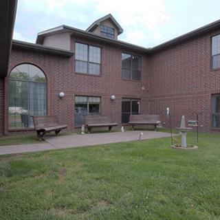 A courtyard with grass, benches, and a wheelbarrow surrounded by a two-story building.