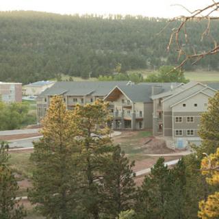 A scenic view of residential buildings nestled among the trees with mountains in the background during sunset.