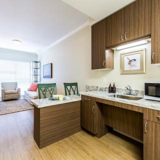 A modern apartment kitchen with wooden cabinets and an adjoining living area.