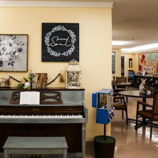 A cozy community space featuring a piano, art on the walls, and seating arrangements for gatherings.