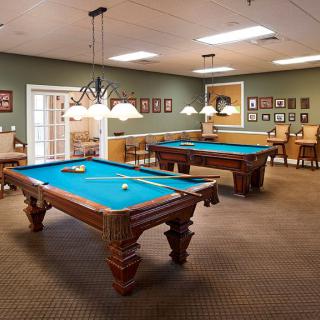 A well-lit game room featuring two billiards tables with blue felt and stylish lighting fixtures.