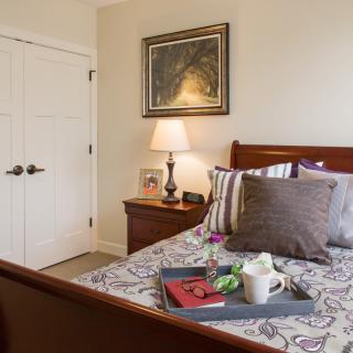 A cozy bedroom with a neatly made bed, featuring decorative pillows, a framed artwork on the wall, and a bedside table with a lamp.