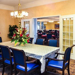 A well-decorated dining room featuring a table with blue chairs and a floral centerpiece, illuminated by an elegant chandelier.