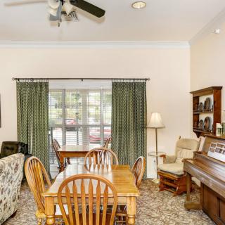 A cozy living room with a dining area, featuring a piano and a set of wooden table and chairs.