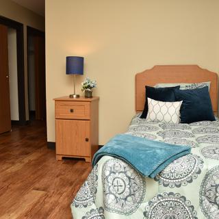 A cozy bedroom with a single bed, bedside table, and lamp on a hardwood floor.
