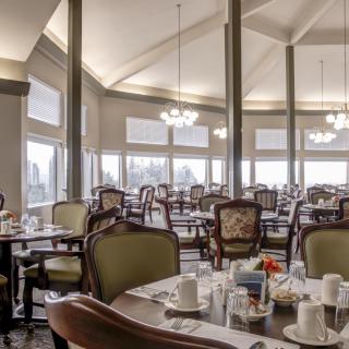 An elegant dining room with neatly arranged tables and chairs, illuminated by chandeliers.