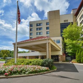 The exterior of a hotel building with a prominent entrance and landscaped surroundings on a sunny day.