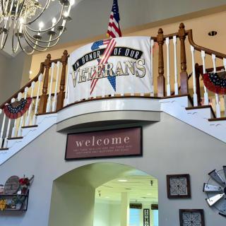 A welcoming interior with a patriotic theme, featuring a banner and elegant chandelier above a staircase.