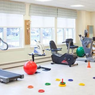 A well-lit gym with various exercise equipment, including a treadmill and stationary bikes.