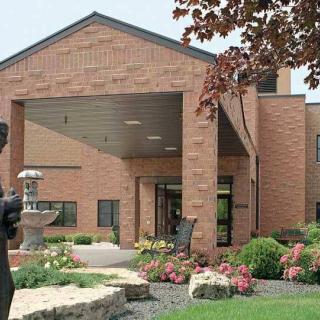 A brick building entrance with landscaped garden and statue.