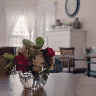 A cozy living room with a vase of flowers on a wooden table, illuminated by natural light.