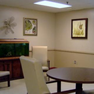 A waiting room featuring chairs, a round table, an aquarium, and framed artwork on the walls.