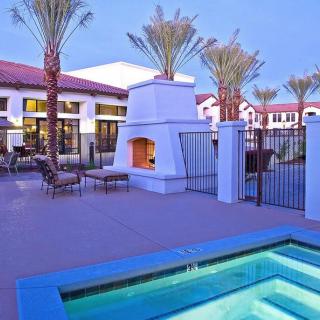 A modern outdoor patio area featuring a swimming pool, fireplace, and palm trees during the evening.