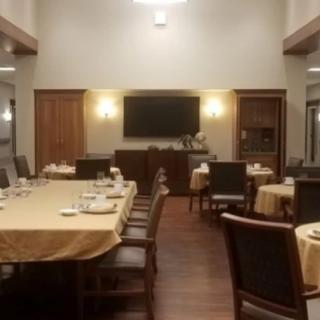 A formal dining room with neatly arranged tables and chairs, featuring a television on the wall.