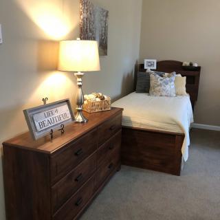 A cozy bedroom with a single bed and wooden dresser, featuring a lamp for ambient lighting.