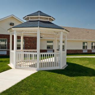 A charming white gazebo nestled in a green lawn, surrounded by a clear blue sky.