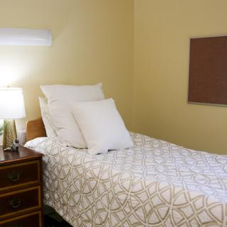 A cozy bedroom featuring a neatly made single bed with decorative pillows, alongside a nightstand and lamp.