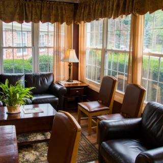 A cozy living room with large windows, leather chairs, and a potted plant.