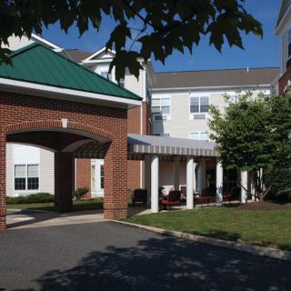 A residential building with a covered entrance and surrounding greenery on a sunny day.