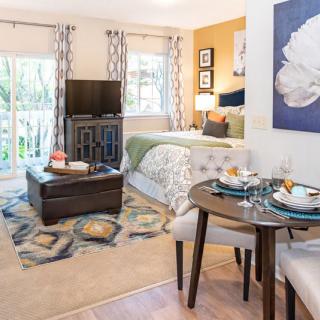 A cozy studio apartment with a combined living and sleeping area, featuring modern decor and a small dining table.