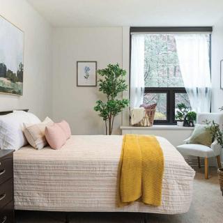A modern bedroom featuring a neatly made bed, artwork on the walls, and a large window with sheer curtains.