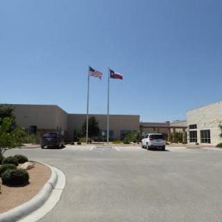 A view of a building with American and state flags flying in front, set against a clear blue sky.