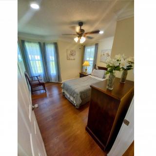 A cozy bedroom with a bed, dresser, ceiling fan, and hardwood flooring.