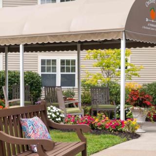 A cozy outdoor seating area featuring benches, colorful flowers, and a shaded awning.
