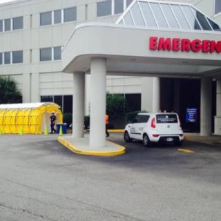 Emergency entrance of a hospital with a yellow tent and parked vehicle.