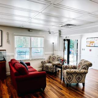 A cozy living room featuring a red couch and patterned chairs, illuminated by natural light.
