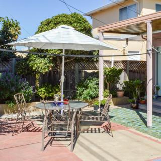 A sunny backyard patio with an umbrella-covered table and chairs, surrounded by a garden.
