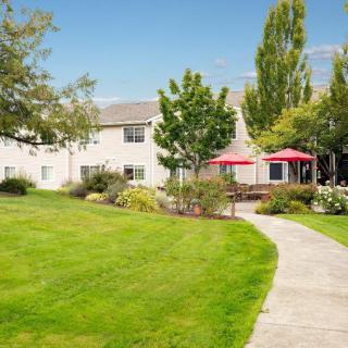 A scenic outdoor garden with a pathway leading to a building, featuring a well-maintained lawn and red patio umbrellas.