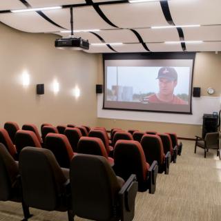 A small movie theater or presentation room with a projection screen and several rows of seats.