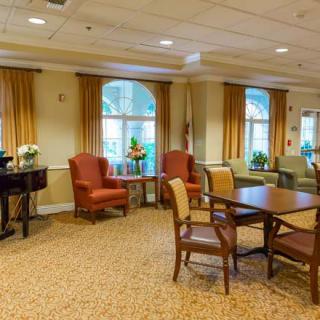 A comfortable seating area with tables and chairs in a carpeted room featuring large windows and curtains.