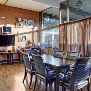 A cozy dining area with a large table, chairs, and a television, complemented by wood flooring and natural light.