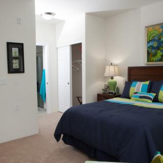 A cozy bedroom featuring a neatly made bed with colorful pillows, a bedside lamp, and decorative artwork on the wall.