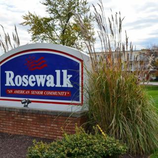 Entrance sign for Rosewalk surrounded by grass and plants.