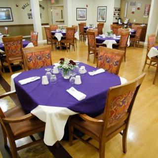 An elegantly set dining area with tables adorned in purple tablecloths and decorative place settings.