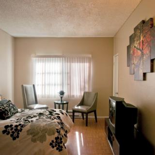 A cozy bedroom with modern furnishings, featuring a bed, chairs, and ample natural light through the window.