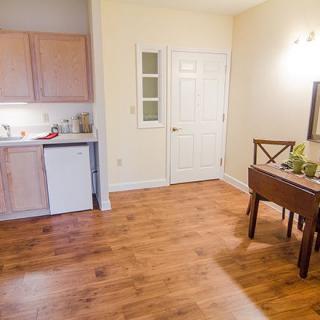 A cozy kitchen and dining area with hardwood floors, featuring a small set of cabinets, a compact fridge, and a dining table with chairs.