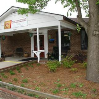 A small brick building with a covered entrance surrounded by greenery and a sidewalk.