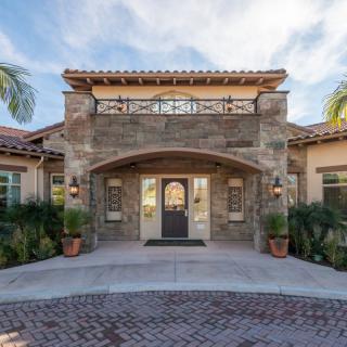 A beautiful house exterior with a stone facade and arched entryway, surrounded by palm trees.