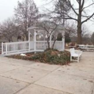 A white gazebo surrounded by bare trees and a bench in a winter landscape.