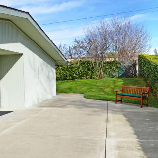 A driveway leading to a garage with a wooden bench beside a grassy area and trees.