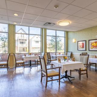 A bright and inviting dining area with neatly arranged tables and chairs, large windows, and decorative artwork on the walls.