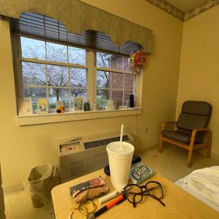 A cozy room with a window view, featuring a table with various items and a comfortable chair.
