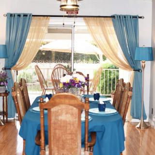 A beautifully arranged dining room with blue tablecloths and curtains, complemented by wooden chairs and abundant natural light.