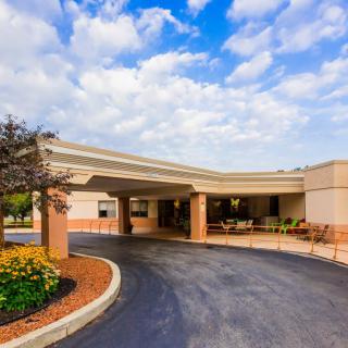 A building entrance with a circular driveway and landscaped surroundings under a cloudy sky.