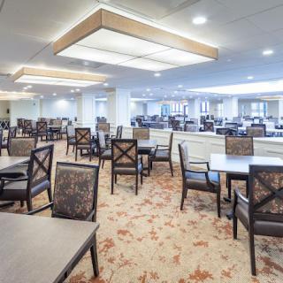 A spacious dining area with modern design, featuring multiple tables and chairs arranged neatly under soft lighting.